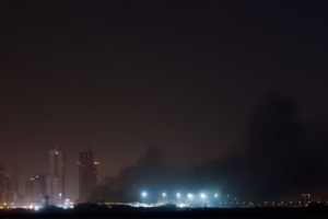 Smoke rising over a city skyline at night following missile or drone strikes